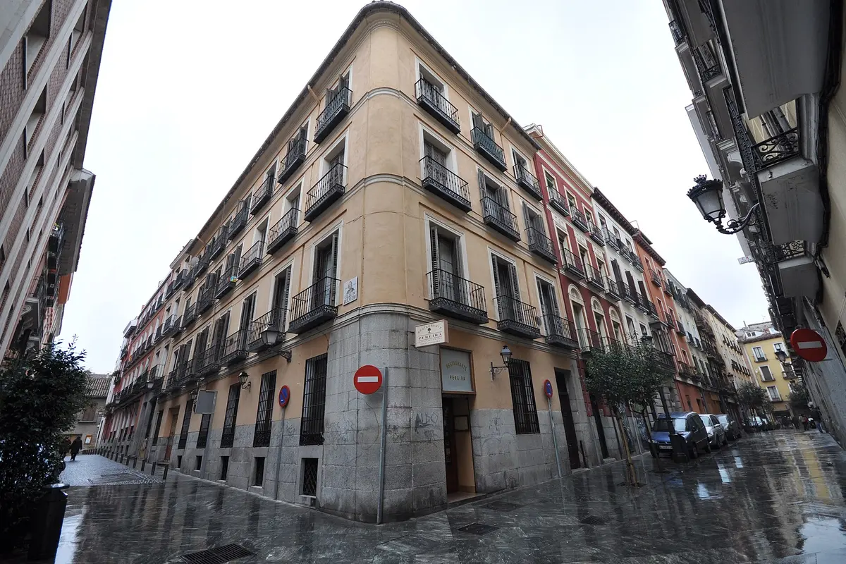 Uma rua pedonal molhada no Barrio de las Letras, em Madrid, com um edifício de esquina cor de damasco, varandas de ferro e carros estacionados ao longo da rua