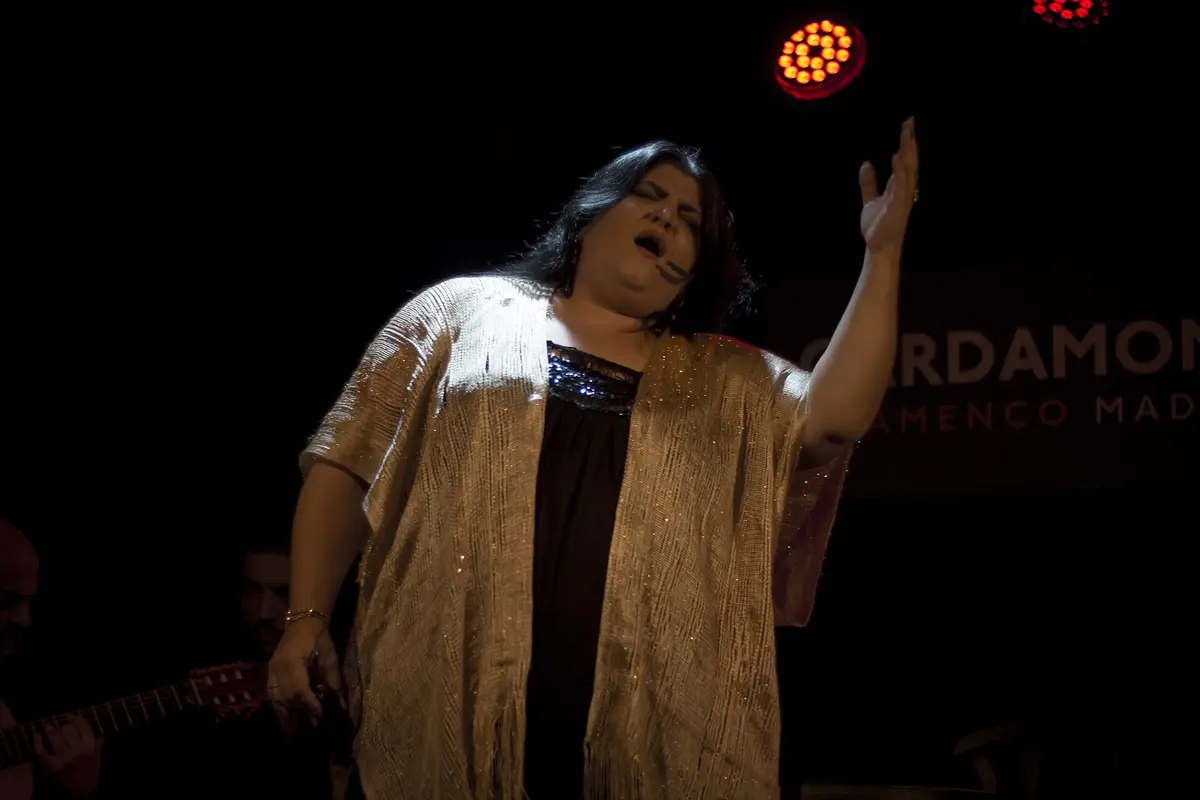 En sanger på scenen på Cardamomo i Madrid, den ene arm løftet, en guitarist delvist synlig til venstre, og spillestedets navn lyser på væggen bagved